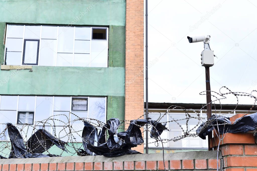 Camera video surveillance on the building background mounted on a brick wall, fenced with barbed wire