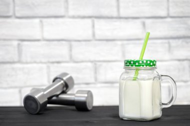 Halterin arka planında beyaz protein kokteyli ve tuğlalarla süslenmiş beyaz bir duvar. Arkaplan