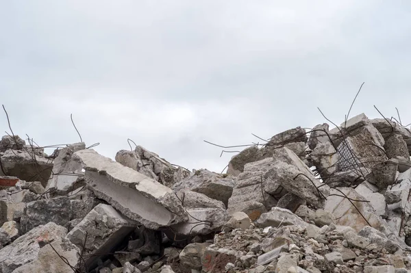 A pile of large gray concrete fragments with protruding fittings against a cloudy sky. — Stock Photo, Image