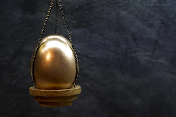 Metal Ovo dourado em uma tigela nas cadeias de escamas em um fundo escuro . — Fotografia de Stock
