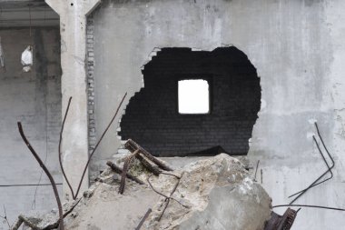 Duvarında bir delik olan büyük bir beton binanın yıkımının kalıntıları ve ön planda takviyeli bir kiriş..
