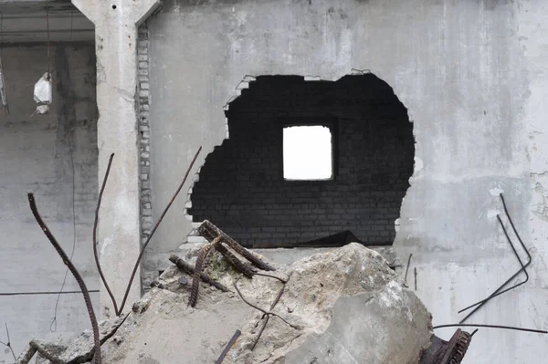 Duvarında bir delik olan büyük bir beton binanın yıkımının kalıntıları ve ön planda takviyeli bir kiriş..