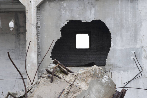 Remnants of the destruction of a large concrete building with a hole in the wall and a beam with reinforcement in the foreground.