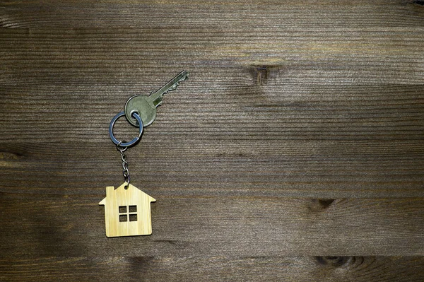 El símbolo de la casa en forma de llavero con una llave de metal sobre un fondo de madera vintage marrón. Copiar espacio . — Foto de Stock