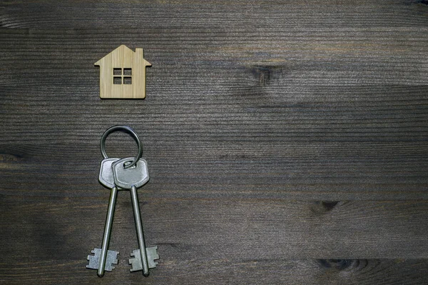 El símbolo de la casa en forma de llavero con llaves de metal sobre un fondo de madera vintage marrón. Copiar espacio . — Foto de Stock