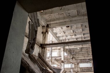Yıkılmış beton yığınlarından, yığılmış levhalardan oluşan büyük bir binanın çerçevesinin içerisinden. Arkaplan