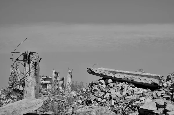 De resten van een verwoest gebouw met betonnen funderingspalen die uit de grond steken. Zwart-witte achtergrond — Stockfoto