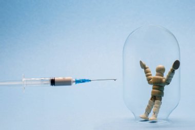 Mavi arka plandaki bağışıklığı sembolize eden cam şişedeki bir adam kendini koronavirüse karşı aşıdan korumaya çalışıyor..