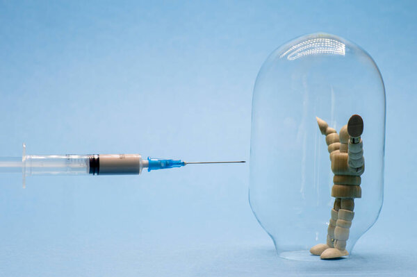 A man in a glass flask symbolizing immunity on a blue background is trying to protect himself from vaccination against coronavirus.