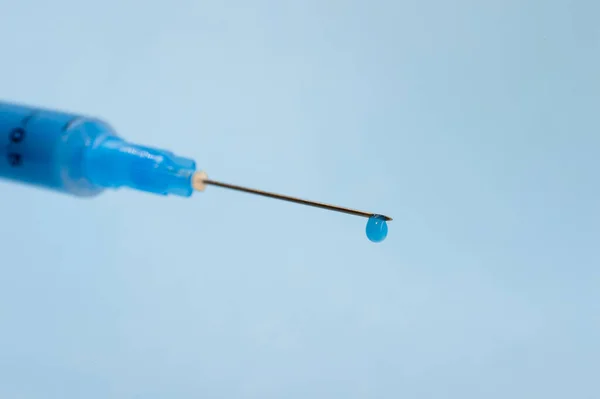 Close-up of a syringe needle with a drop of solution at the end on a blue background.