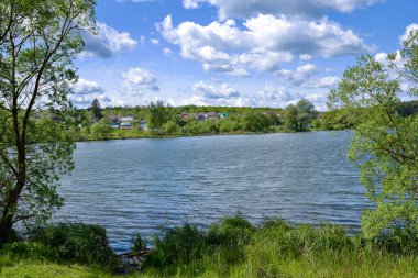 Yazlık bir göl manzarası ve beyaz bulutlu mavi bir gökyüzü ve uzak bir köy. Arkaplan.