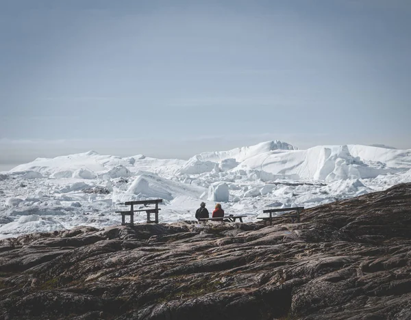 Twee mensen zitten met uitzicht op Icefjord in Ilulissat. Gemakkelijke wandelroute naar de beroemde Kangia gletsjer in Groenland. De Ilulissat Icefjord gezien vanuit het gezichtspunt. — Stockfoto