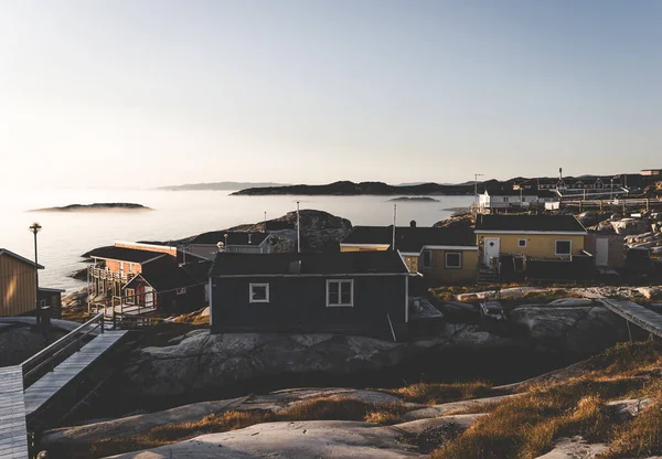 Vista aérea da cidade ártica de Ilulissat, Groenlândia durante o pôr-do-sol com nevoeiro. Casas coloridas no centro da cidade com icebergs no fundo no verão em um dia ensolarado com laranja rosa — Fotografia de Stock