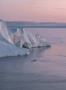 Grönland 'da buzdağlarıyla kutup manzarası gece yarısı güneş batarken ufukta güneş batıyor. Gece yarısı mevsimi boyunca sabah erken saatlerde alpenlight. Ilulissat, Batı Grönland.