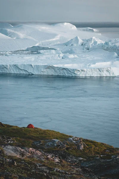 Wieczorna scena w Ilulissat z widokiem na Kangia Icefjord z namiotem i pływającymi górami lodowymi w pochmurny dzień — Zdjęcie stockowe