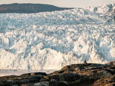 Kocaman buzdan bir duvar. Grönland 'daki Eqip Sermia Buzulu Eqi buzuluna gece yarısı güneşi altında buzul yavrusu denir. Gezi ve tatil sırasında yürüyüşçüler.