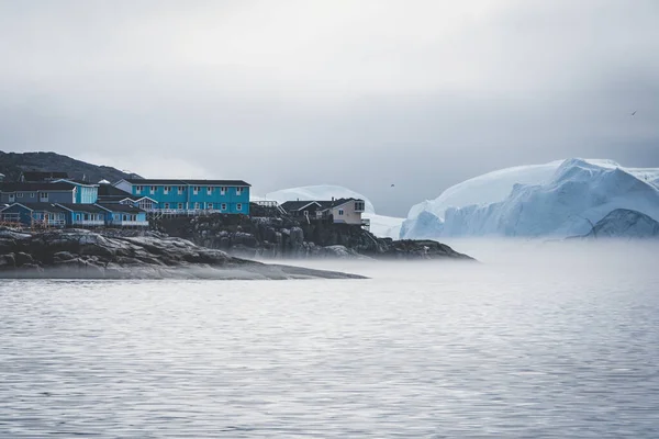 Grönland, Ilulissat 'ın Arktik şehrinin hava manzarası gün doğumunda sisle kaplandı. Kasabanın merkezinde renkli evler, yaz aylarında arka planda buzdağları, turuncu pembe ve güneşli bir günde. — Stok fotoğraf