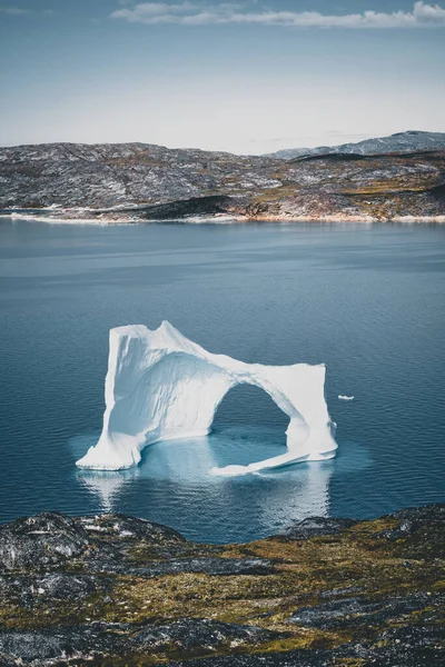 Isberg med valv i Antarktis Grönlands vatten mot bakgrund av fjällen på Arktiska halvön. Små färgglada hus på en solig dag med blå himmel och moln. — Stockfoto