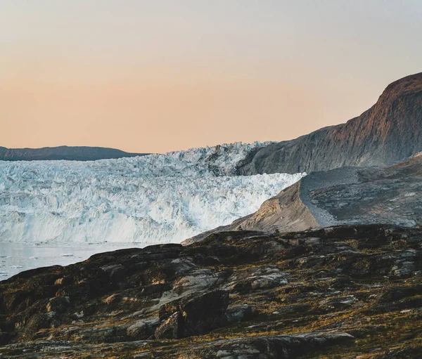 Menschen, die vor einer riesigen Gletscherwand aus Eis sitzen. eqip sermia glacier eqi glacier in Grönland, der kalbende Gletscher während der Mitternachtssonne. Wanderer auf Reisen und im Urlaub. — Stockfoto