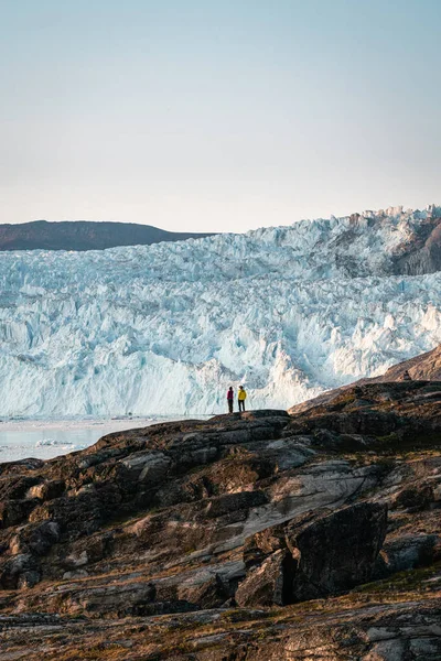 Люди сидять навпроти величезної крижаної стіни. Льодовик Екіп Сермія Екі в Гренландії назвав відколювання льодовика під час полярного сонця. Мандрівники під час подорожей і відпусток. — стокове фото