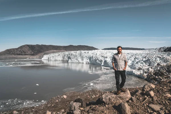 Un joven turista viajero de pie frente al glaciar Eqip Sermia llamado Glaciar Eqi. Pared de hielo en el fondo. El concepto de calentamiento global y guías profesionales. En un día soleado con cielo azul —  Fotos de Stock