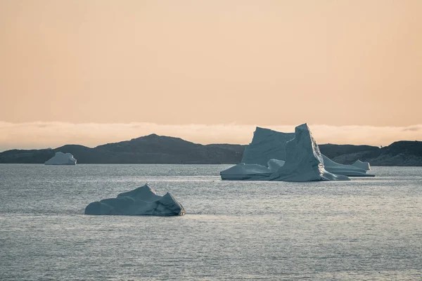 夕阳西下的冰山 格陵兰的自然和地貌。 迪斯科湾 西格陵兰岛 仲夏夜太阳和冰山 冰块中的蓝色大冰。 受气候变化和全球变暖影响的国家. — 图库照片