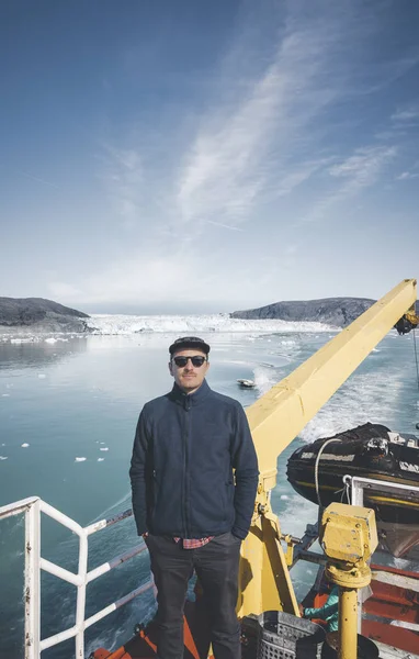 En ung man resenär turist står framför Eqip Sermia glaciär som heter Eqi Glacier. Vägg av is i bakgrunden. Begreppet global uppvärmning och professionella guider. På en solig dag med blå himmel — Stockfoto