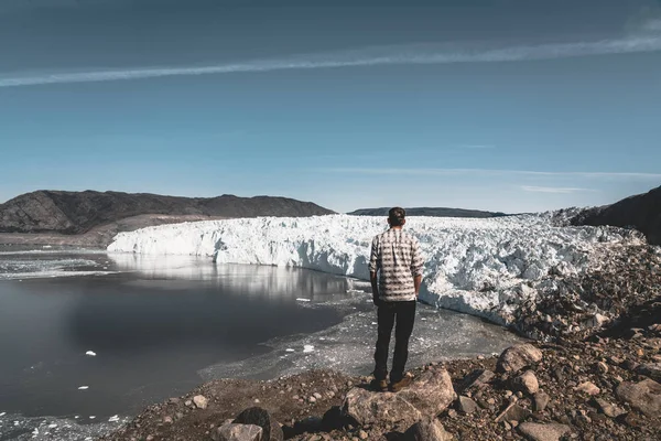 En ung man resenär turist står framför Eqip Sermia glaciär som heter Eqi Glacier. Vägg av is i bakgrunden. Begreppet global uppvärmning och professionella guider. På en solig dag med blå himmel — Stockfoto