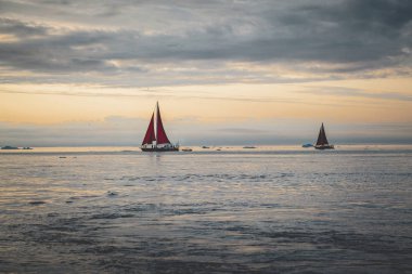 Kuzey kutbunda, ölçeği gösteren devasa bir buzdağının yanında güzel kırmızı yelkenli. Polar yaz Ilulissat, Disko Körfezi gece yarısı güneş sezonu sırasında Disko Körfezi buzul yüzen buzdağları arasında seyir