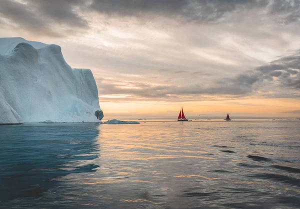 Belo veleiro vermelho no Árctico ao lado de um iceberg maciço mostrando a escala. Cruzeiro entre icebergs flutuantes na geleira Disko Bay durante a meia-noite sol temporada de verão polar Ilulissat, Disko Bay — Fotografia de Stock