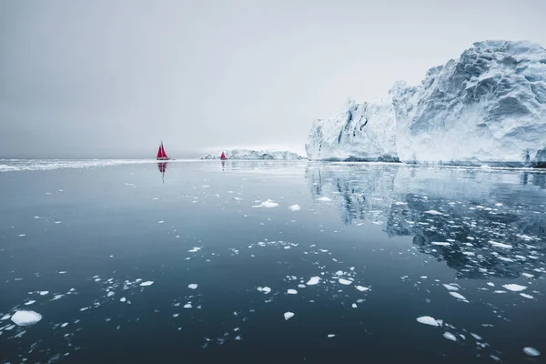 Kuzey kutbunda, ölçeği gösteren devasa bir buzdağının yanında güzel kırmızı yelkenli. Polar yaz Ilulissat, Disko Körfezi gece yarısı güneş sezonu sırasında Disko Körfezi buzul yüzen buzdağları arasında seyir — Stok fotoğraf