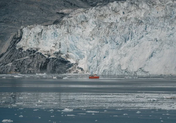 Rotes Passagier-Kreuzfahrtschiff, das durch die eisigen Gewässer des grönländischen Qasigiannguit segelt, mit dem Eqip sermia eqi Gletscher im Hintergrund. Eis bricht vom kalbenden Gletscher ab. Ein kleines Boot inmitten von Eisbergen — Stockfoto