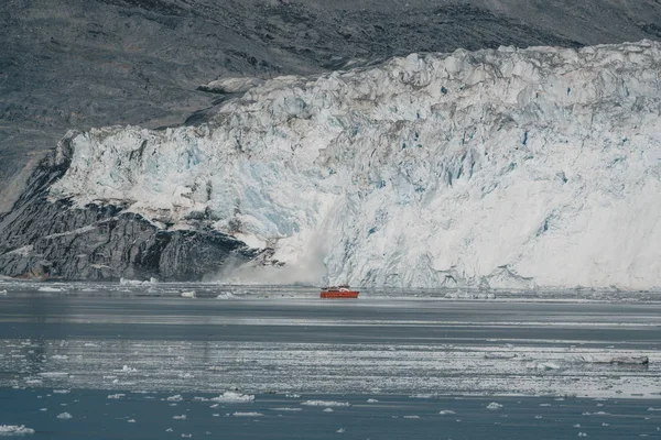 Red Passenger cruise ship sailing through the icy waters of Qasigiannguit, Greenland with Eqip Sermia Eqi Glacier in Background. Ice breaking off from calving glacier. A small boat among icebergs