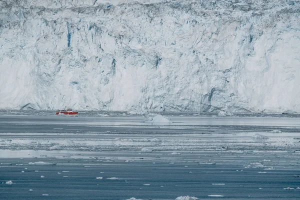 Nave da crociera Red Passenger che naviga attraverso le acque ghiacciate di Qasigiannguit, Groenlandia con il ghiacciaio Eqip Sermia Eqi sullo sfondo. Una piccola barca tra gli iceberg. Crociera in barca a vela tra iceberg galleggianti — Foto Stock