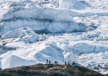 İnsanlar buzdan dev bir duvarın önünde oturuyorlar. Icefjord Ilulissat. Grönland 'daki Jakobshaven Eqip Sermia Buzulu Eqi buzuluna gece yarısı güneşi altında buzul yavrusu denir. Yürüyüşçüler