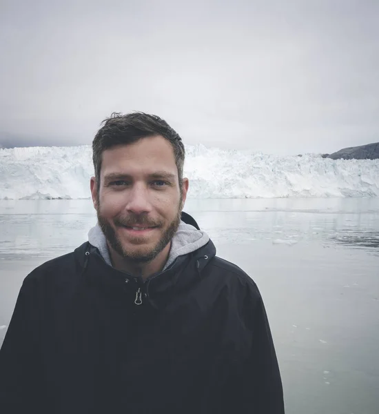 Young traveler tourist sitting standing in front of huge glacier wall of ice. Icefjord Ilulissat. Jakobshaven Eqip Sermia Glacier Eqi glacier in Greenland called the calving glacier during midnight