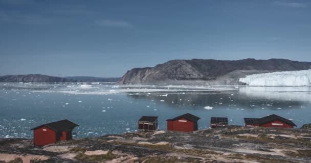 4k em movimento Timelapse Video clip of Eqip Sermia Glacier Eqi glaciar huts in Greenland called the calving glacier during day with blue sky and sun. Parede de gelo geleira enorme. Grandes pedaços de gelo a cair — Vídeo de Stock