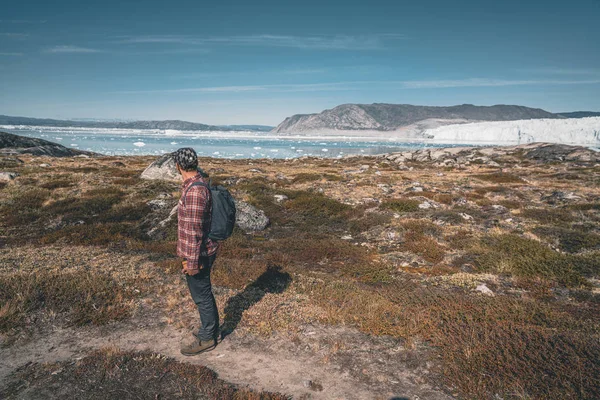 Un joven turista viajero de pie frente al glaciar Eqip Sermia llamado Glaciar Eqi. Pared de hielo en el fondo. El concepto de calentamiento global y guías profesionales. En un día soleado con cielo azul —  Fotos de Stock