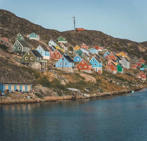 Casas coloridas pontilham as encostas da cidade piscatória de Kangaamiut, Gronelândia Ocidental. Icebergs do glaciar Kangia na Groenlândia nadando com céu azul e nuvens. Símbolo do aquecimento global . — Fotografia de Stock