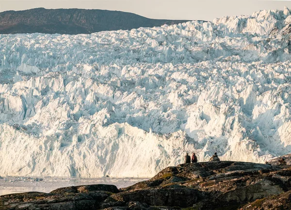 Mensen die voor een enorme gletsjermuur van ijs zitten. Eqip Sermia Gletsjer Eqi gletsjer in Groenland wordt de kalvende gletsjer genoemd tijdens middernachtzon. Wandelaars tijdens reis en vakantie. — Stockfoto