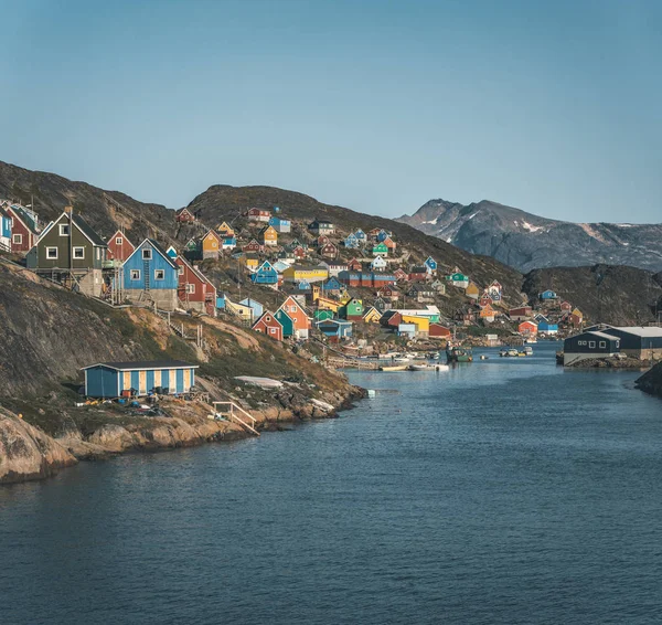 Kleurrijke huizen op de hellingen van de vissersstad Kangaamiut, West-Groenland. IJsbergen van Kangia gletsjer in Groenland zwemmen met blauwe lucht en wolken. Symbool van opwarming van de aarde. — Stockfoto