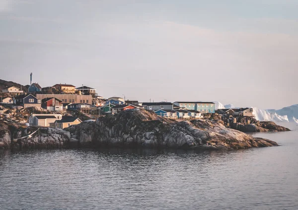 Vista aérea da cidade ártica de Ilulissat, Groenlândia durante o pôr-do-sol com nevoeiro. Casas coloridas no centro da cidade com icebergs no fundo no verão em um dia ensolarado com laranja rosa — Fotografia de Stock