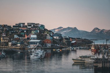 Grönland 'daki Maniitsoq Arctic City' nin gün batımı manzarası. Gece yarısı güneşi altında arka planda dağlar. Renkli evler ve panorama. Gemilerle limana bak.