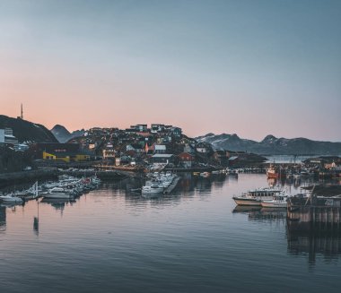 Grönland 'daki Maniitsoq Arctic City' nin gün batımı manzarası. Gece yarısı güneşi altında arka planda dağlar. Renkli evler ve panorama. Gemilerle limana bak.