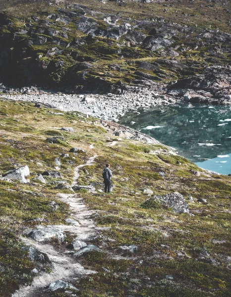 Utsikt mot isfjorden i Ilulissat. Ung man resenär turist står på strandpromenaden. Isberg från Kangias glaciär på Grönland simmar med blå himmel och moln. Symbol för global uppvärmning. — Stockfoto