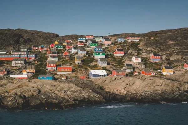 西格陵兰Kangaamiut渔镇的山坡上点缀着五彩斑斓的房屋。 格陵兰坎吉亚冰川的冰山带着蓝天和蓝云在游泳。 全球变暖的标志. — 图库照片