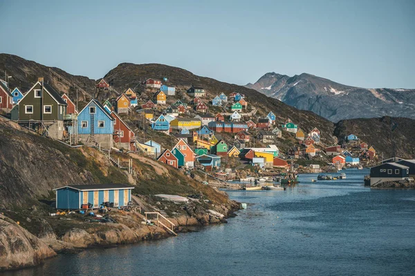 Casas coloridas pontilham as encostas da cidade piscatória de Kangaamiut, Gronelândia Ocidental. Icebergs do glaciar Kangia na Groenlândia nadando com céu azul e nuvens. Símbolo do aquecimento global . — Fotografia de Stock