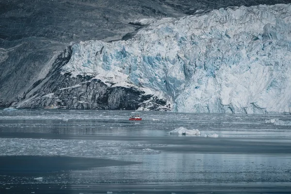 Crucero de pasajeros rojo navegando a través de las aguas heladas de Qasigiannguit, Groenlandia con el glaciar Eqip Sermia Eqi en segundo plano. Un pequeño barco entre icebergs. Velero de crucero entre icebergs flotantes —  Fotos de Stock
