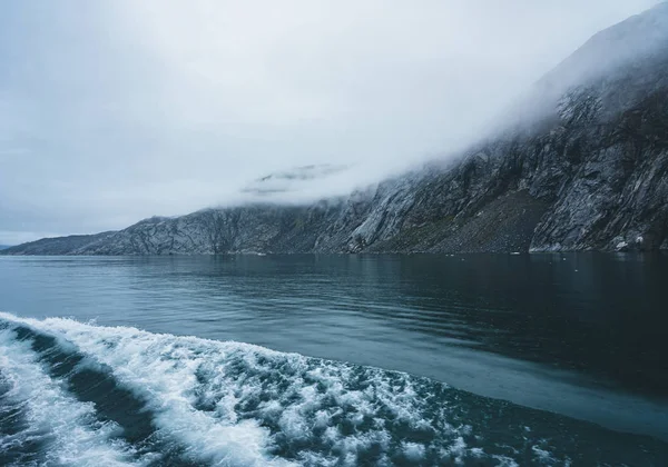 Golven storten neer aan de kust op een bewolkte dag in de poolcirkel in Groenland. Krachtige oceaangolven breken, golven breken op een ondiepe oever. Natuurlijke achtergrond met wolken hangen laag in de — Stockfoto