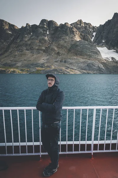 Joven guapo mirando hacia adelante y sonriendo mientras está de pie en la cubierta de un barco en el Ártico. A bordo del buque costero Sarfaq Ittuk en Groenlandia que viaja de Ilulissat a Nuuk . —  Fotos de Stock